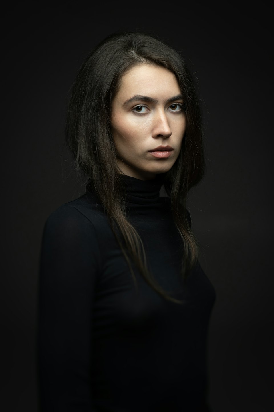 Mujer de pelo largo y oscuro con jersey negro de cuello alto.