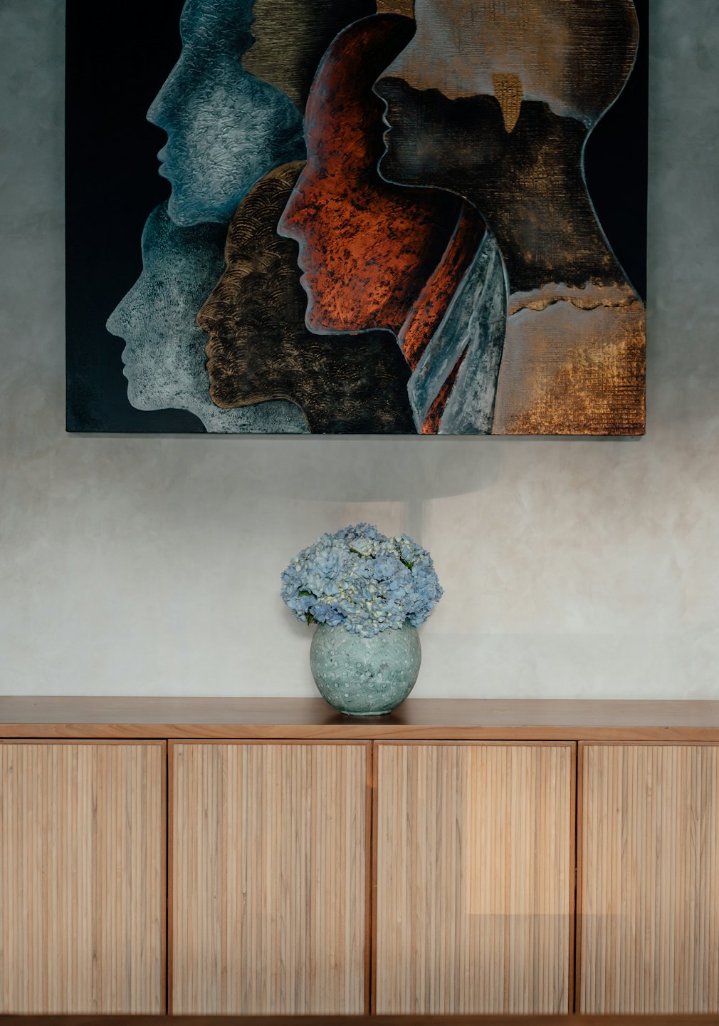 Pintura abstracta de perfiles humanos sobre un mueble de madera con hortensias.